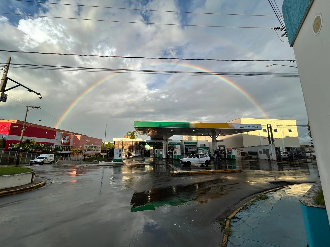 Pista do Posto São Paulo 3 em Batatais logo depois da chuva, com um arco-íris completo sobre a cobertura verde e amarela.